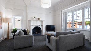 A modern living room with a fireplace, a flat-screen TV, and a large window offering a view of the outside. - 1913 on Vincent Soaring ceilings and stunning Views (Daylesford)