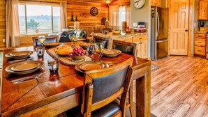 A wooden interior with a dining table set for a meal, a kitchen area with wooden cabinets, and a large clock on the wall.