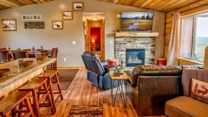 A cozy cabin interior with a stone fireplace, wooden furniture, and a dining area.