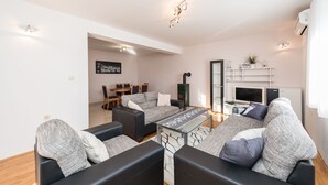 Een moderne woonkamer met een zithoek, een salontafel en een open haard. Achtergrond toont een eethoek met een tafel en stoelen.