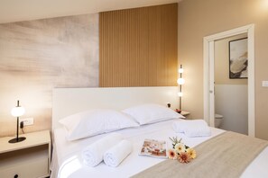 Une chambre d’hôtel avec un grand lit, deux lampes de chevet, une table de chevet, une porte et un luminaire fixé au mur.