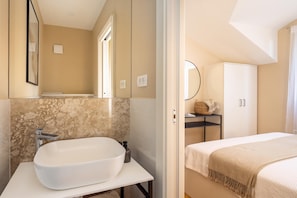 Een moderne badkamer met een grote witte wastafel, een spiegel en een marmeren achterwand.