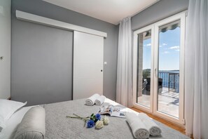 A bedroom with a bed, a window, and a view of a balcony.