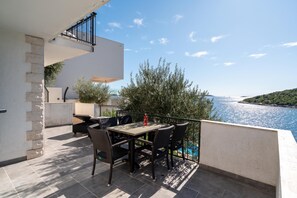 Un balcon avec une table et des chaises, donnant sur une étendue d’eau et sur de la verdure.