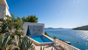 A modern pool area with a clear view of the sea, surrounded by rocks and plants. - Pool Villa Sine /w Panoramic Sea View, Trogir - Vinišće, Croatia (Trogir - Vinišće)
