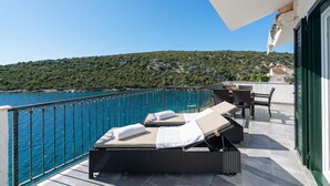 A balcony with wicker furniture, a table, and chairs overlooking a body of water and a hilly landscape. - Pool Villa Sine /w Panoramic Sea View, Trogir - Vinišće, Croatia (Trogir - Vinišće)