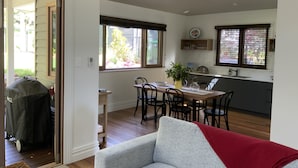 A modern kitchen with a dining area, wooden flooring, and large windows. - Charming Luxury Self Contained Cottage. (Leura)