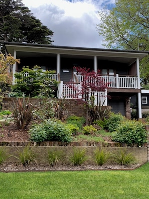 A two-story house with a covered porch, a brick wall, and a garden with various plants and shrubs.