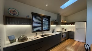 A modern kitchen with a central island, dark cabinetry, a built-in oven, and a white refrigerator. - Charming Luxury Self Contained Cottage. (Leura)