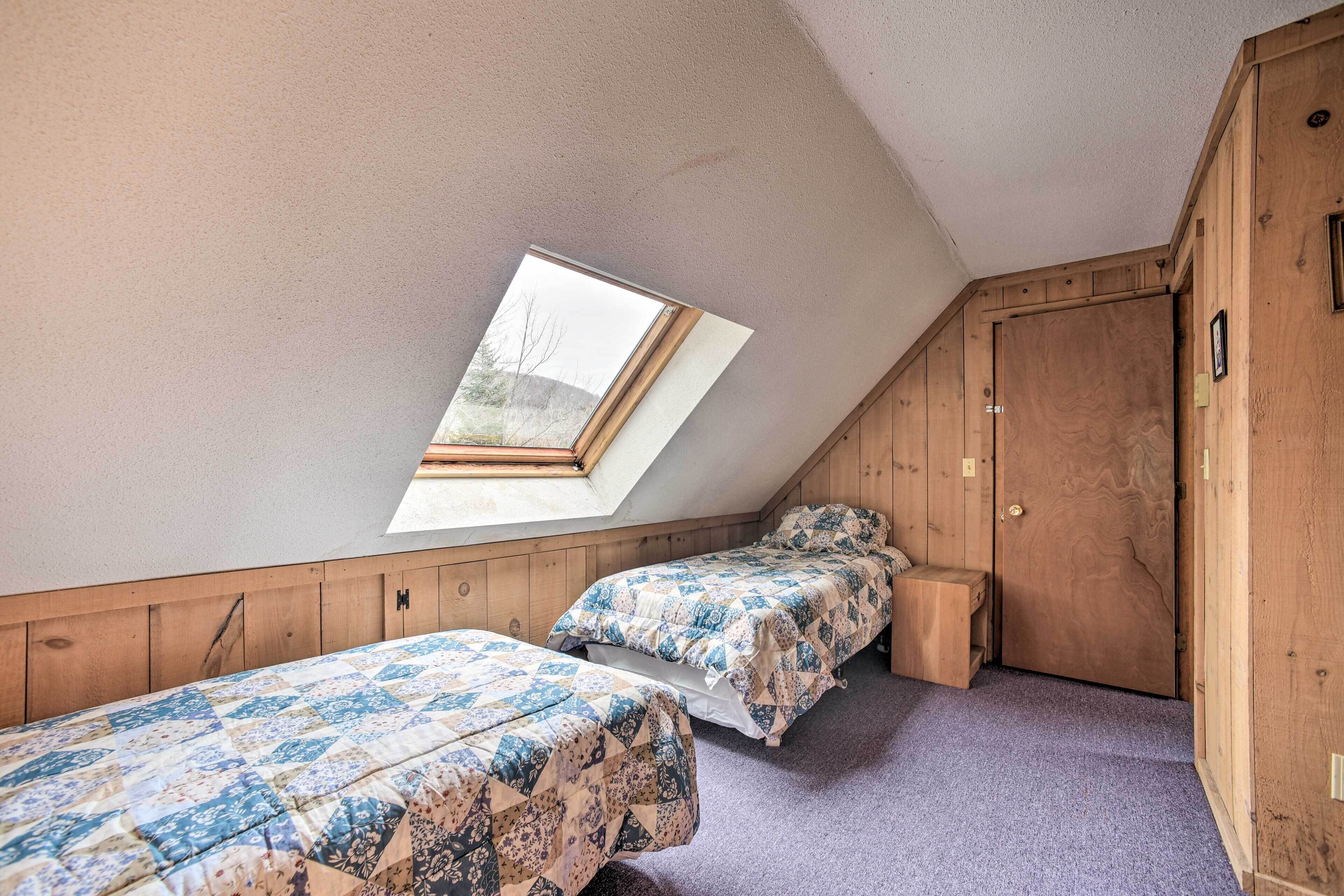 A room with two beds, a skylight, wooden walls, and a door.