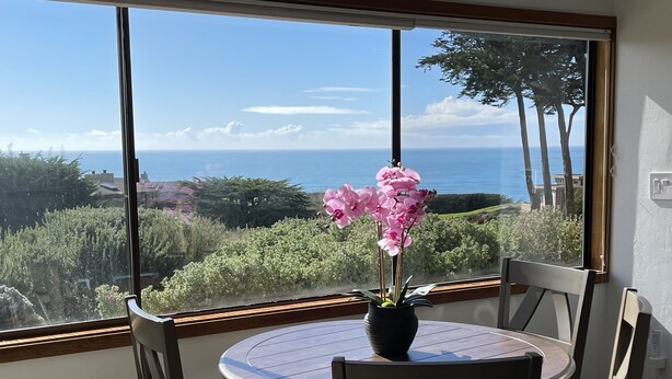 A dining area with a table and chairs, a potted orchid, and a view of the ocean through large windows. - Ocean & Golf Fairway view (Bodega Bay)