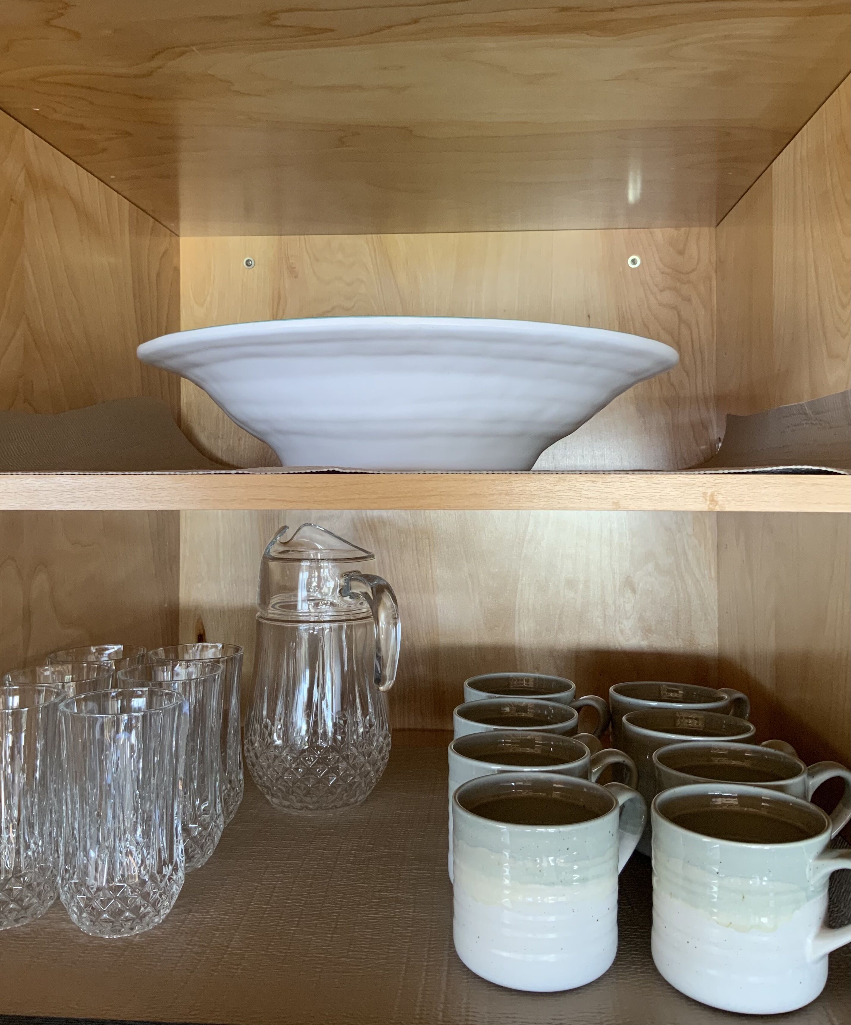 A wooden shelf with a white bowl, a crystal pitcher, and several glass mugs.