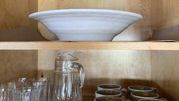 A wooden shelf with a white bowl, a crystal pitcher, and several glass mugs.