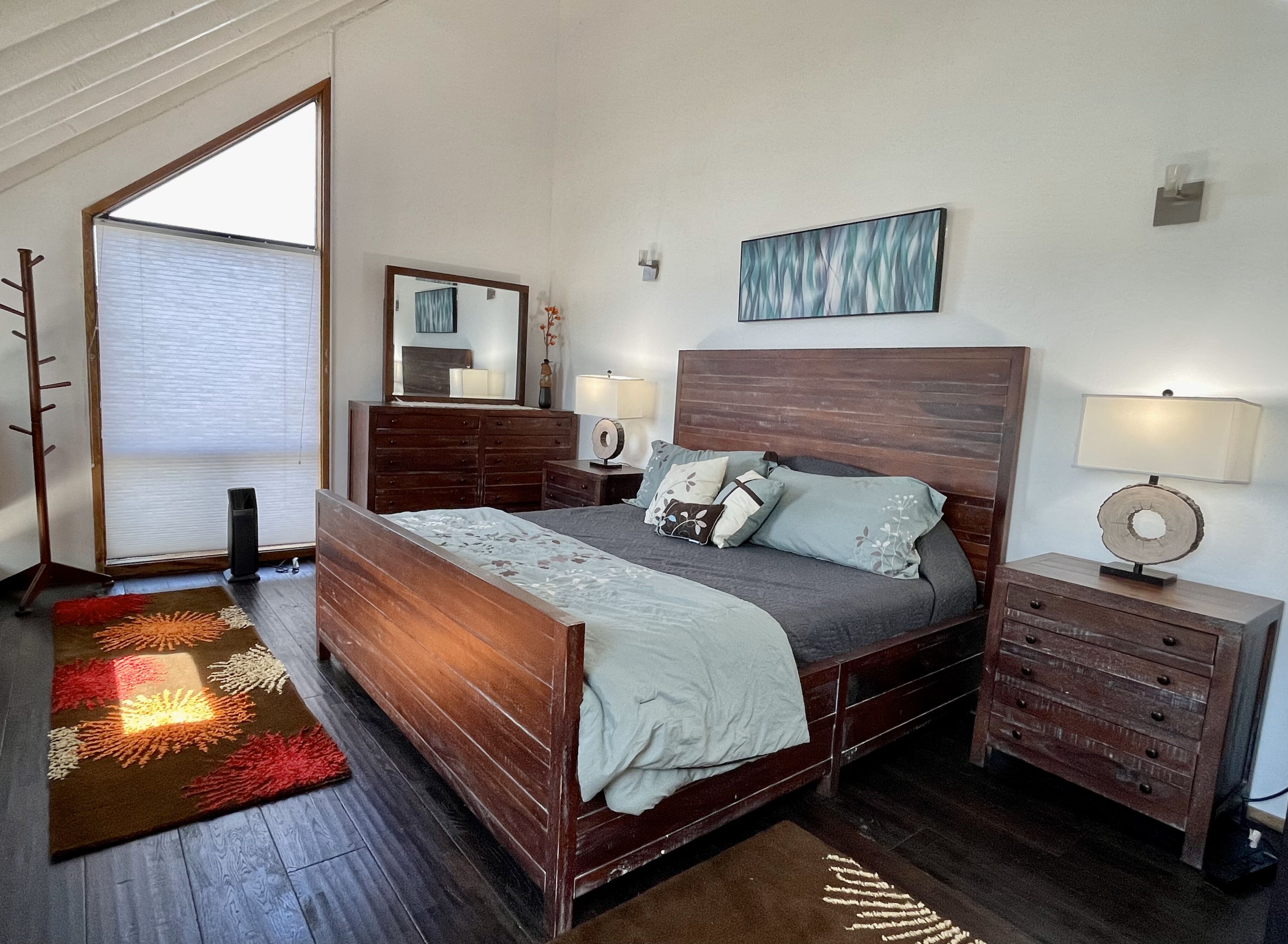 Une chambre à coucher avec un lit en bois, une commode, un miroir et une table de chevet avec une lampe.