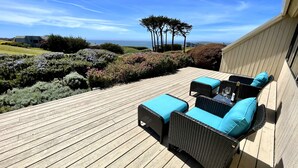 A wooden deck with wicker furniture and cushions, overlooking a landscaped garden and ocean view. - Ocean & Golf Fairway view (Bodega Bay)