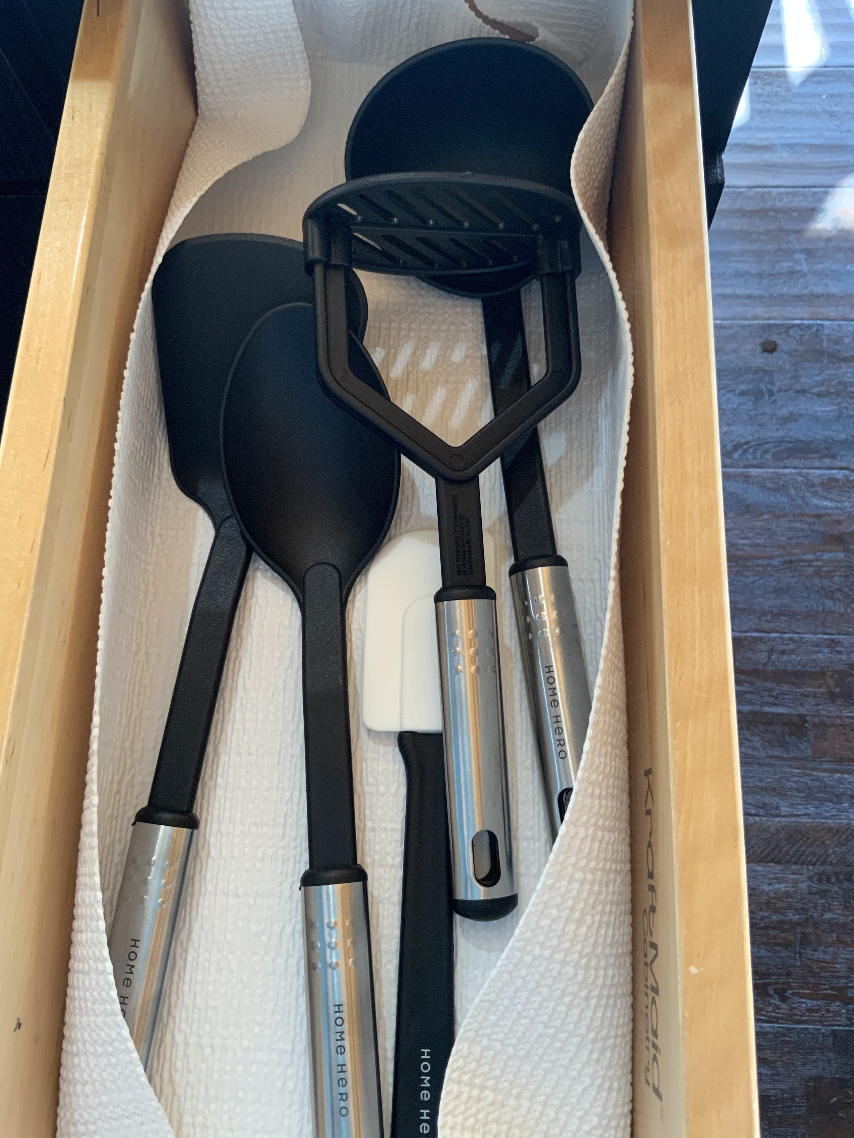 A drawer containing a set of kitchen utensils, including a spatula, a ladle, and a pair of tongs, all with black handles and silver accents.