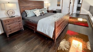A bedroom with a wooden bed, bedside tables, a wall-mounted artwork, and a view of the adjacent room. - Ocean & Golf Fairway view (Bodega Bay)