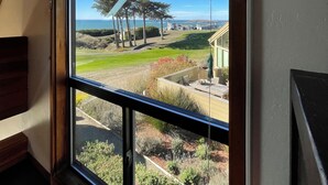 A view from a window with a clear sky, a wooden structure, and a landscaped area with plants and a building in the distance. - Ocean & Golf Fairway view (Bodega Bay)