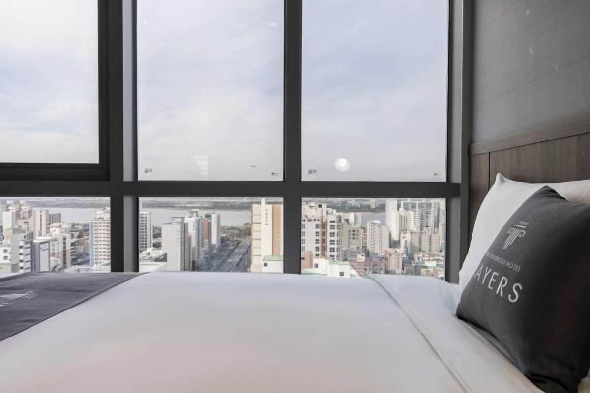 A hotel room with a large window, a bed, and a pillow with text.