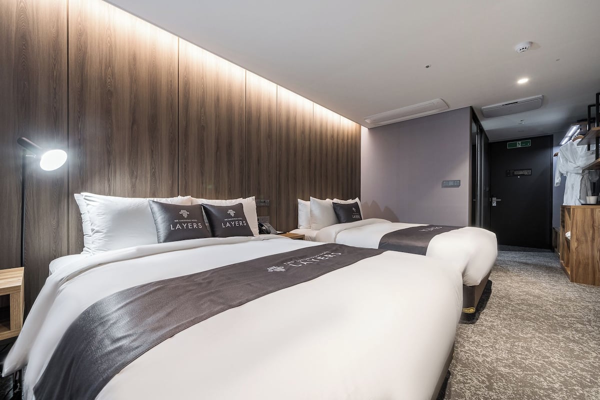 A hotel room with two beds, a wooden panel wall, a small desk, and a wardrobe.