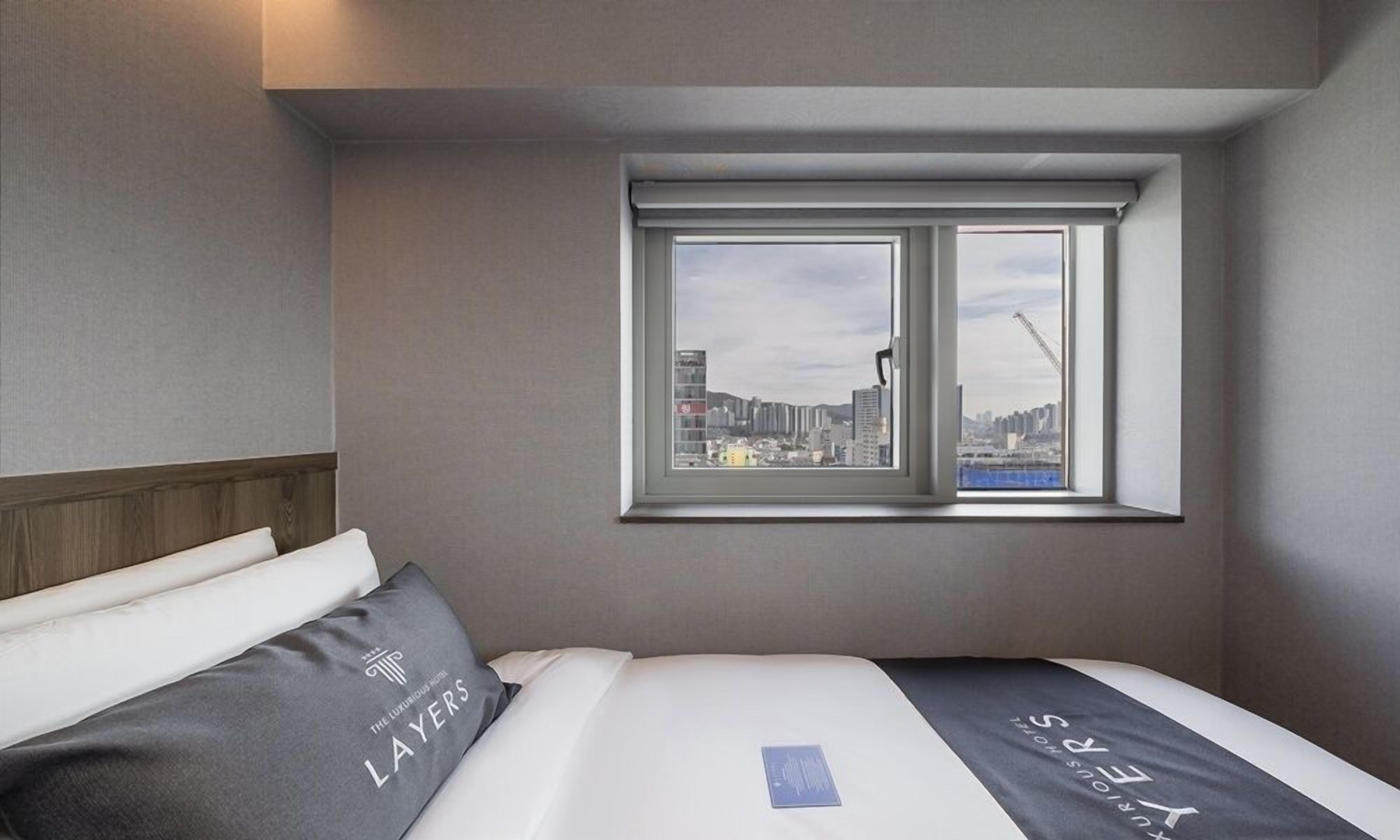 A hotel room with a bed, pillows, and a window with a city view.