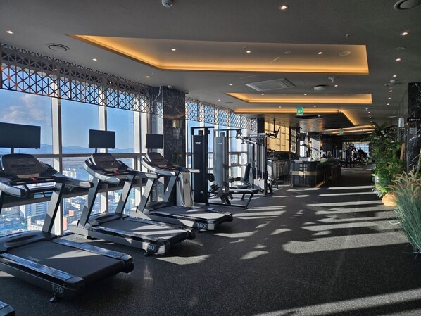 A modern gym with treadmills, weight machines, and a view of the city.