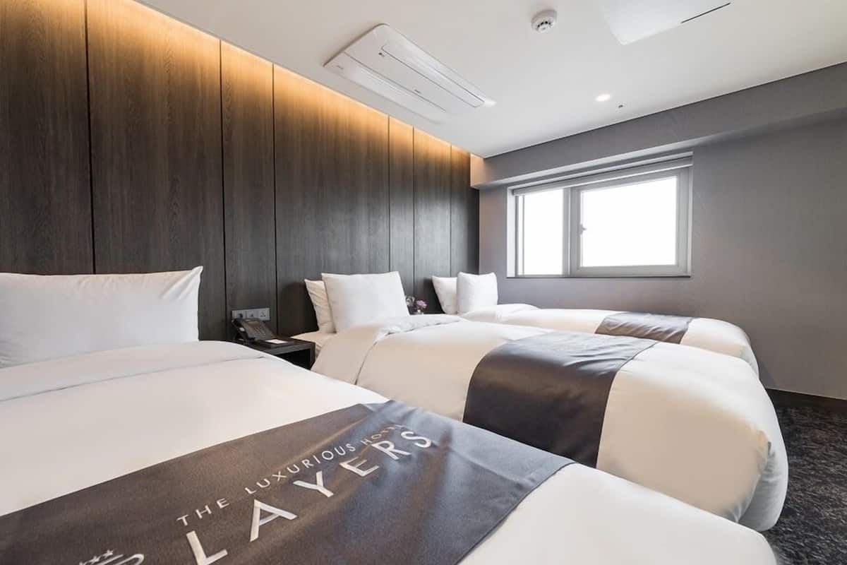 A hotel room with two beds, a nightstand, a phone, and a window.