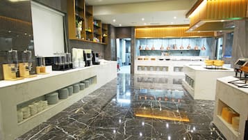 A modern hotel lobby with marble flooring, a reception desk, and a kitchen area visible in the background.