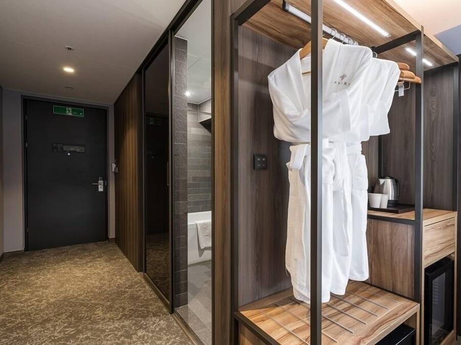 A hotel room with a wooden vanity, a robe hanging on a rack, and a shower area.