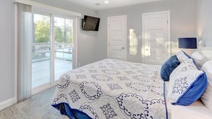 A bedroom with a ceiling fan, a bed with patterned bedding, a TV mounted on the wall, and a sliding glass door leading to an outdoor area. - Heated Pool Access | 5*Clean | Flex Cancelation (Tybee Island)