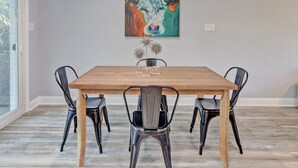 A dining area with a wooden table and four chairs. A colorful painting of a cow is on the wall above the table. - Heated Pool Access | 5*Clean | Flex Cancelation (Tybee Island)