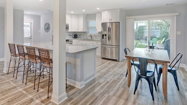 A modern kitchen with white cabinets, a stainless steel refrigerator, and a dining area with a wooden table and chairs. - Heated Pool Access | 5*Clean | Flex Cancelation (Tybee Island)