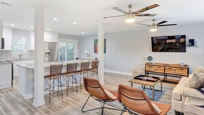 A modern open-plan living space with a kitchen, dining area, and seating area. - Heated Pool Access | 5*Clean | Flex Cancelation (Tybee Island)