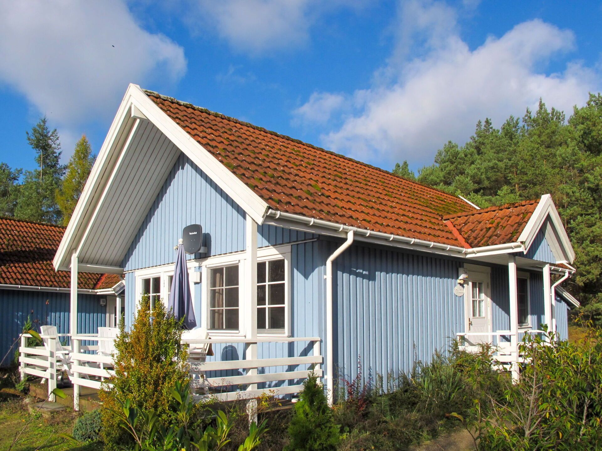 Uma casa de madeira azul com telhado de telhas vermelhas, detalhes brancos e varanda com cadeiras brancas.