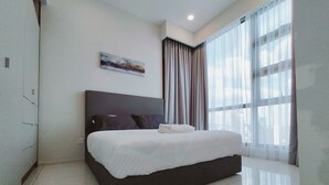 A modern hotel room with a large bed, a painting on the wall, and a view of the city through large windows.