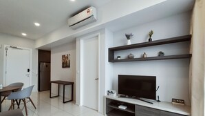 A modern living room with a flat-screen TV, a dining area with a table and chairs, and a built-in entertainment unit with shelves.