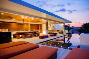 Et moderne udendørs loungeområde med pool, siddepladser og bar.