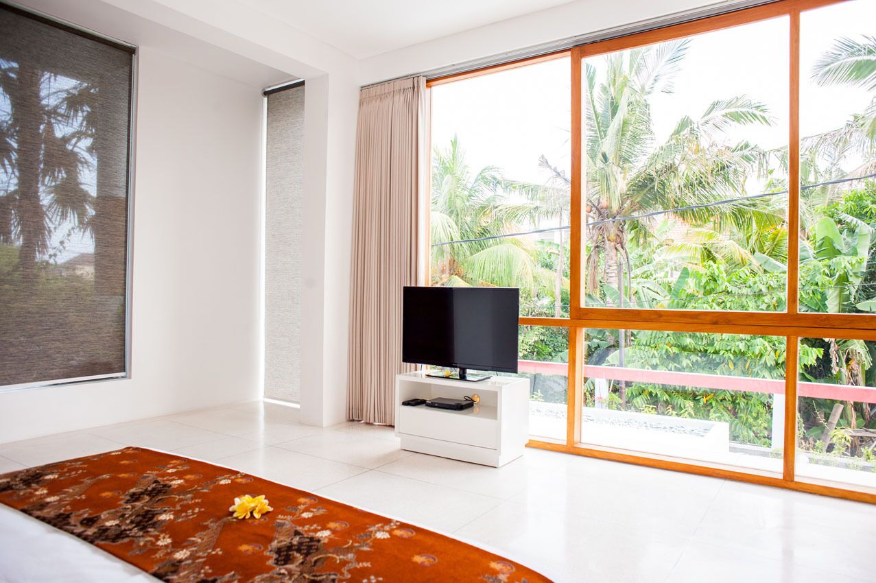 A modern bedroom with a large window, a flat-screen TV, a bed with a floral bedspread, and a white bedside table.