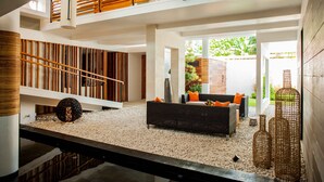 Amplio espacio interior con diseño moderno, que presenta un sofá negro con cojines naranjas, una escalera de madera y un techo de listones de madera.
