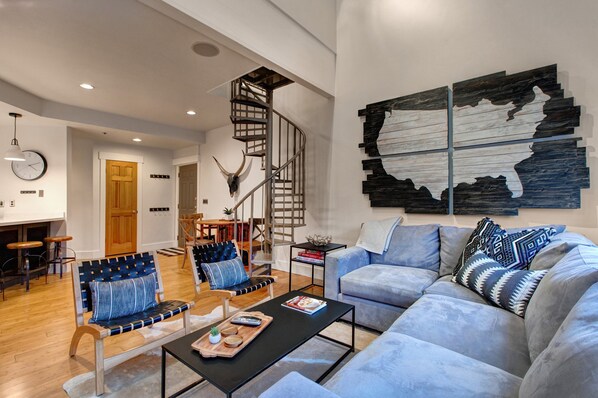 Un salon moderne avec un escalier, un canapé, une table basse et un coin repas.
