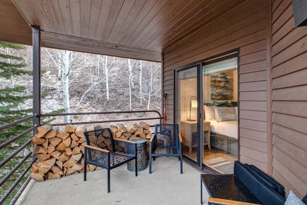 A covered outdoor area with a stack of firewood, two chairs, and a table.