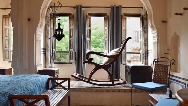Ein Zimmer mit einem großen Rundbogen, einem Schaukelstuhl, einem blauen Sofa und einem Holztisch.