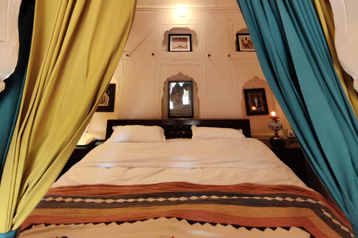 A bed with a patterned bedspread, curtains, and framed pictures on the wall.