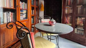 Ein Zimmer mit einem runden Tisch, einem Stuhl mit Sitzkissen und einem Bücherregal voller Bücher.