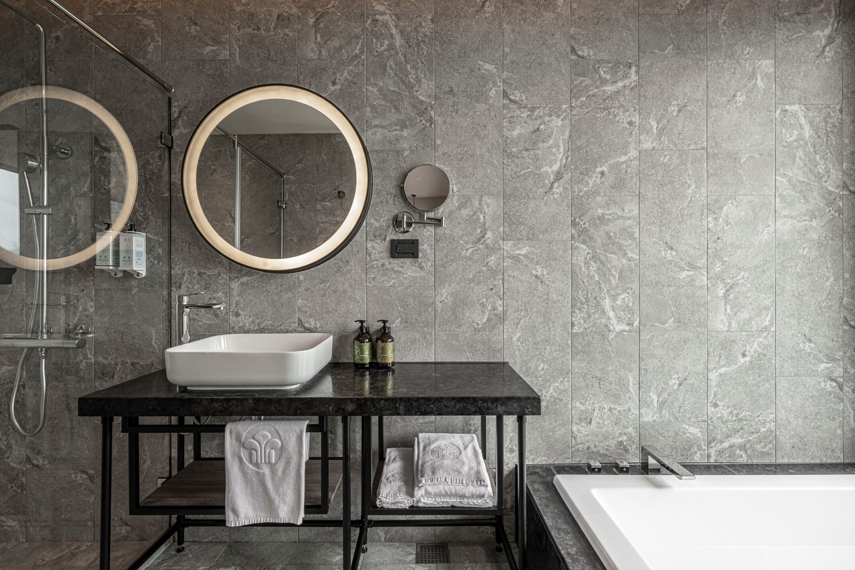A modern bathroom with a large sink, two mirrors, a bathtub, and a shower.