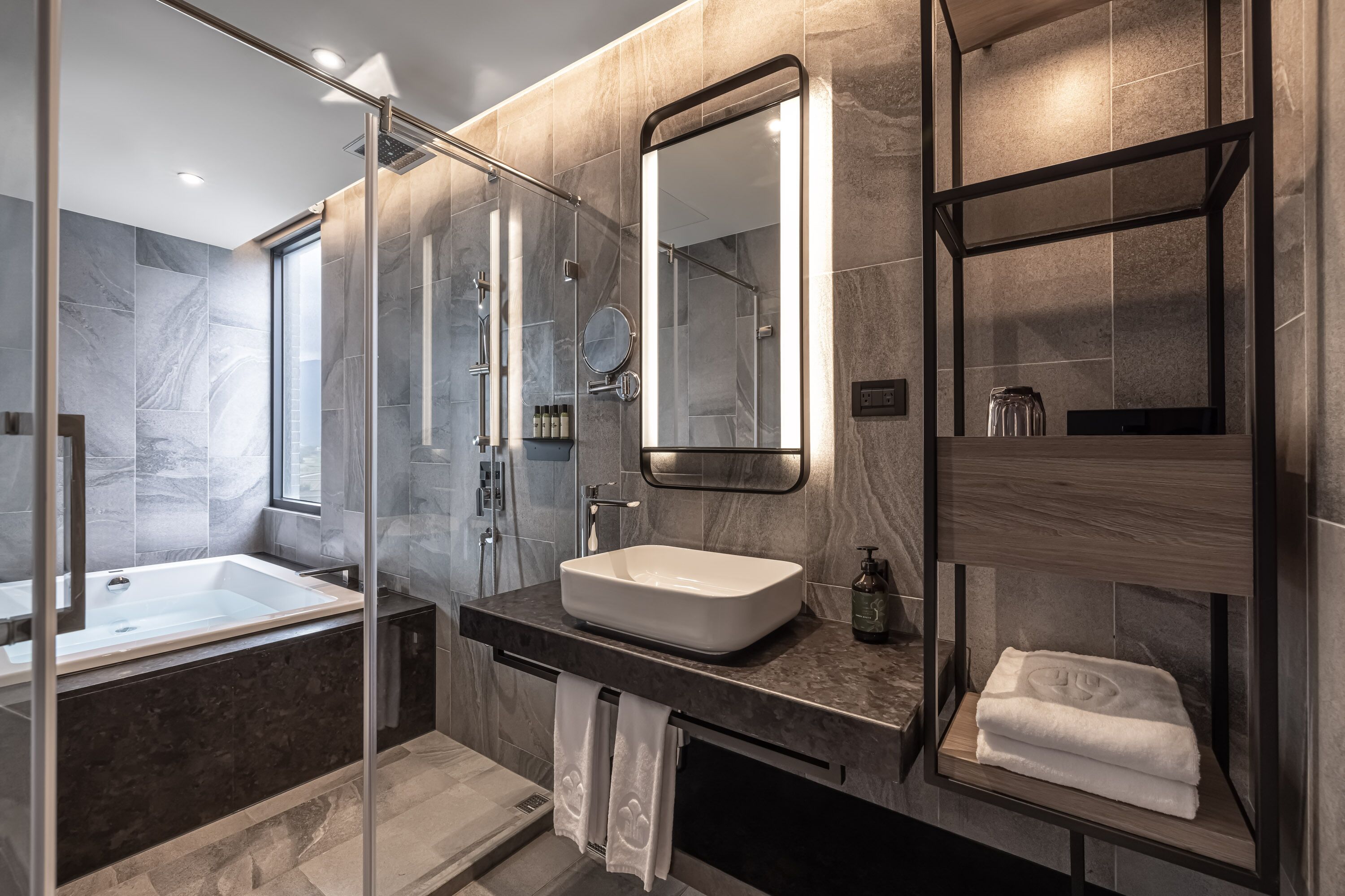 Un baño moderno con ducha envuelta en vidrio, un espejo grande y un lavamanos empotrado.