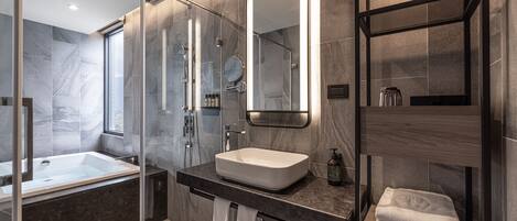 Un baño moderno con ducha envuelta en vidrio, un espejo grande y un lavamanos empotrado.