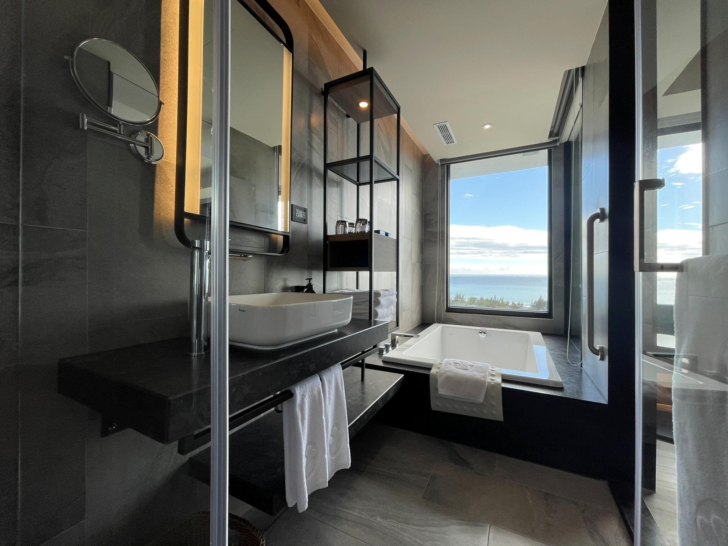 A modern bathroom with a large window, a bathtub, and a vanity with a sink.