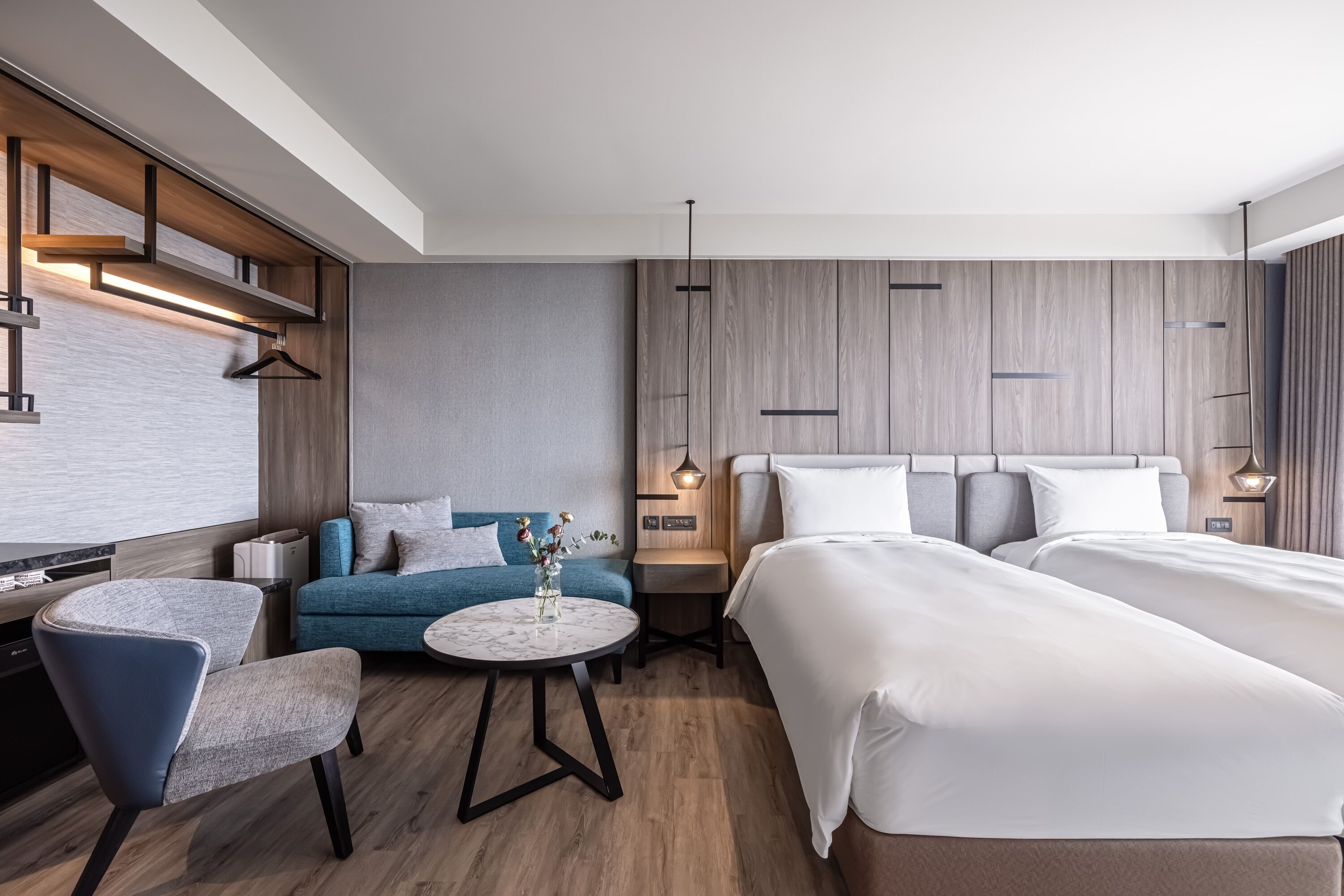 Una habitación de hotel moderna con una cama, un sofá, una silla, una mesita pequeña y un perchero.