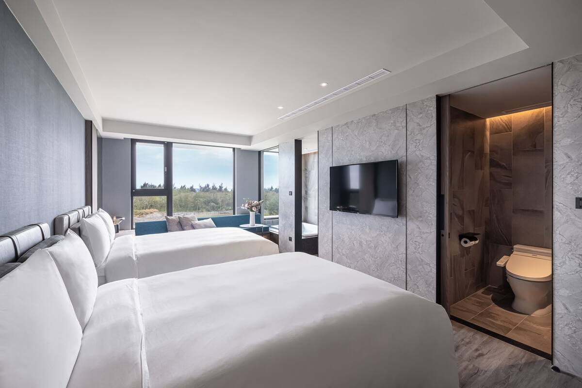 A modern hotel room with two large beds, a flat-screen TV, and a bathroom with a marble finish.